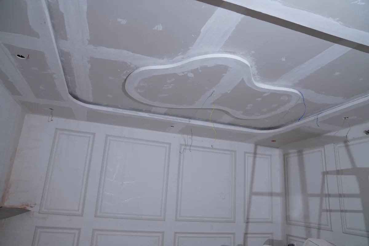 Gypsum false ceiling with curved cove above moulded wall panels, at putty stage