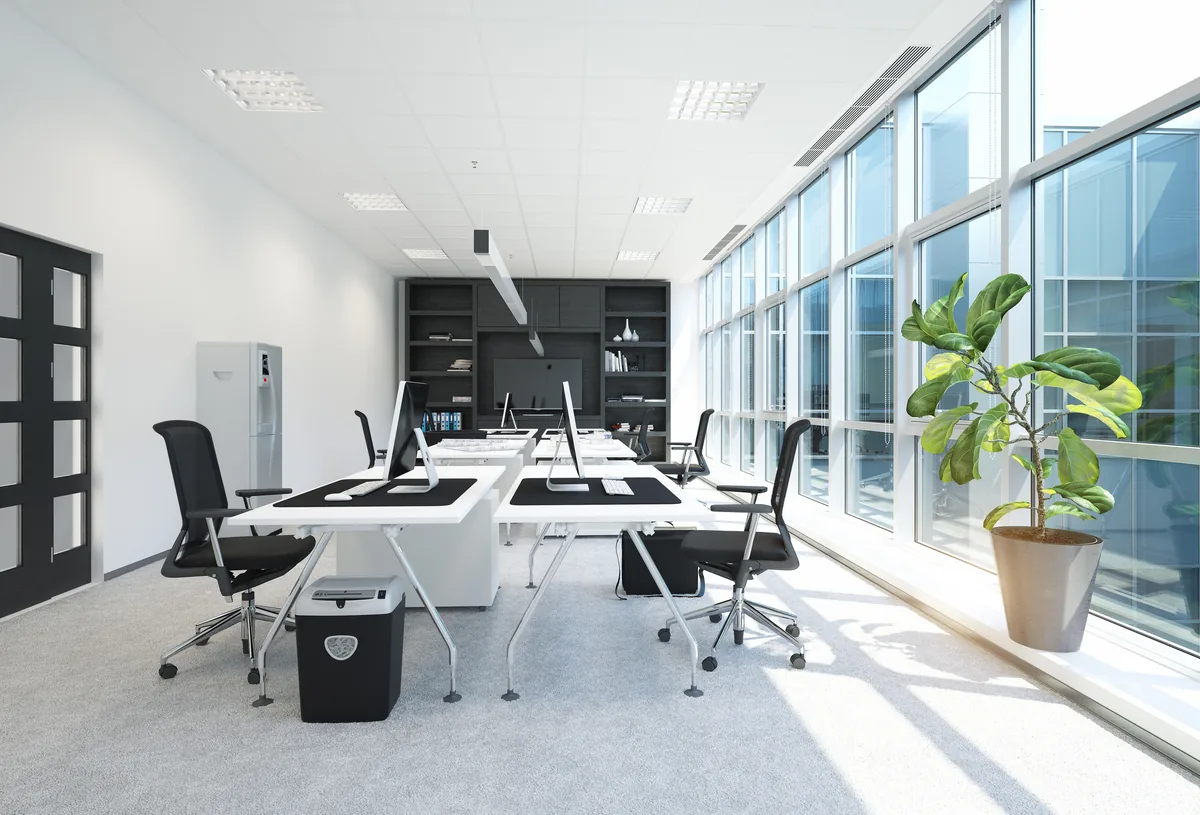 Bright office with white desks beside a wall of windows